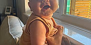 Henry joined the competition — help win amazing prizes! baby, child, infant, sitting, couch, window, indoor, hand, person, smiling, sunlight, home, arm, face, skin, clothing, warm_light, cozy, window_frame, furniture