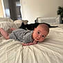 Henry is registered to the contest to win money with this photo: baby, infant, bed, striped_clothing, looking, curious, indoors, soft_light, dog, black_dog, blurred_background, white_bedspread, person, face, head, skin, child, resting, candid, home