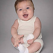 Astin is registered to the contest to win money with this photo: baby, blue_eyes, child, cream_outfit, cross_legged, cute, happy, infant, isolated, light_skin, neutral_background, playful, portrait, short_hair, sitting, small, smiling, studio, white_socks, young