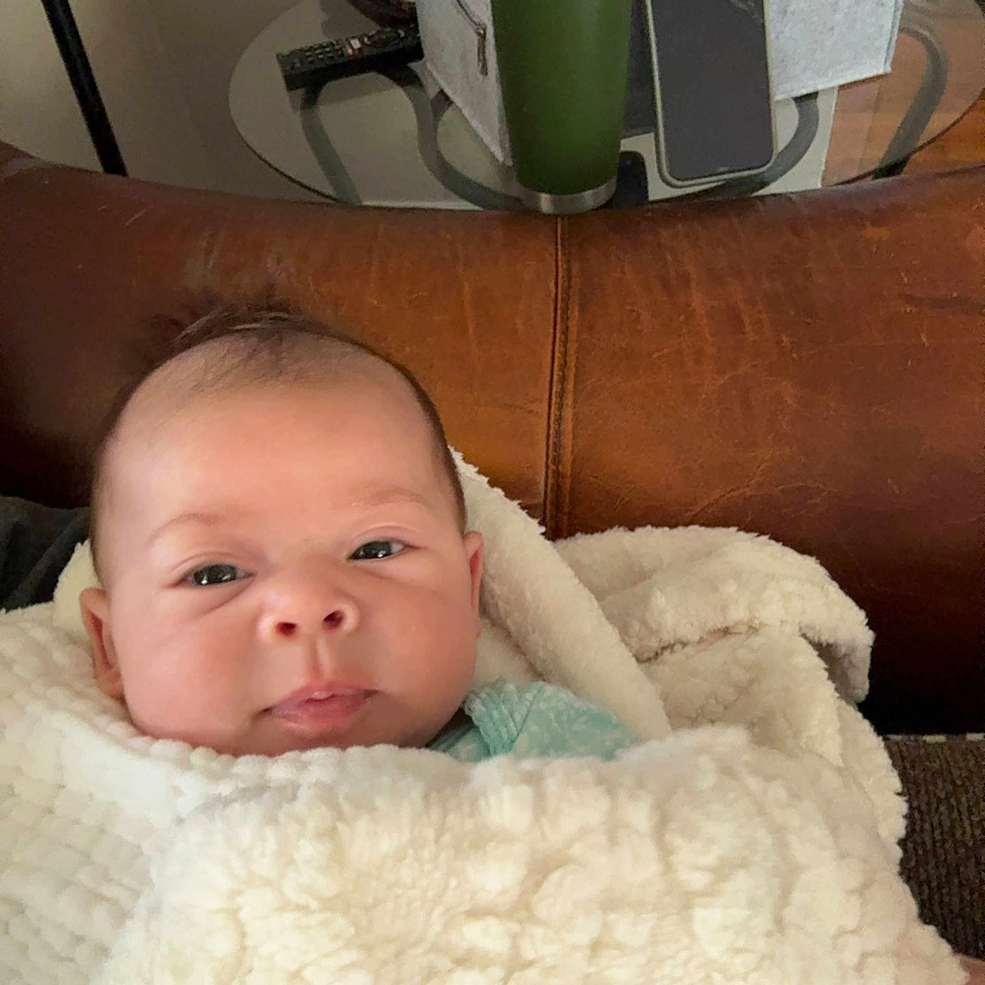 Myahlynn joined the competition — help win amazing prizes! baby, blanket, face, infant, leather_couch, remote_control, table, curious, indoor, cozy, portrait, child, wrapped, soft_texture, home, young, pout, seated, closeup, furniture