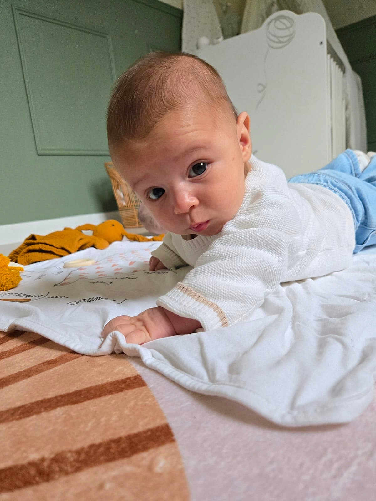 Jude a rejoint le concours — aidez-le/la à gagner de superbes lots ! baby, infant, tummy_time, blanket, toy, crib, white_sweater, blue_jeans, floor, indoor, child, cute, portrait, looking_at_camera, hand, head, skin, expression, room, soft_lighting