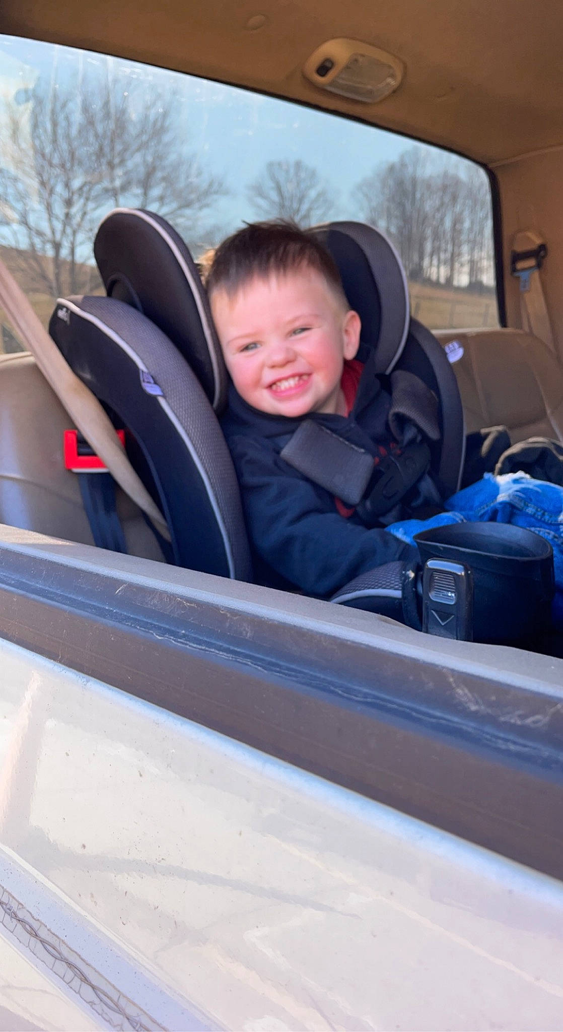 Jd is registered to the contest to win money with this photo: auto_part, automotive_design, automotive_exterior, automotive_mirror, car_seat, car_seat_cover, face, hood, joy, mode_of_transport, motor_vehicle, person, personal_luxury_car, sky, smile, steering_part, steering_wheel, toddler, tree, vehicle