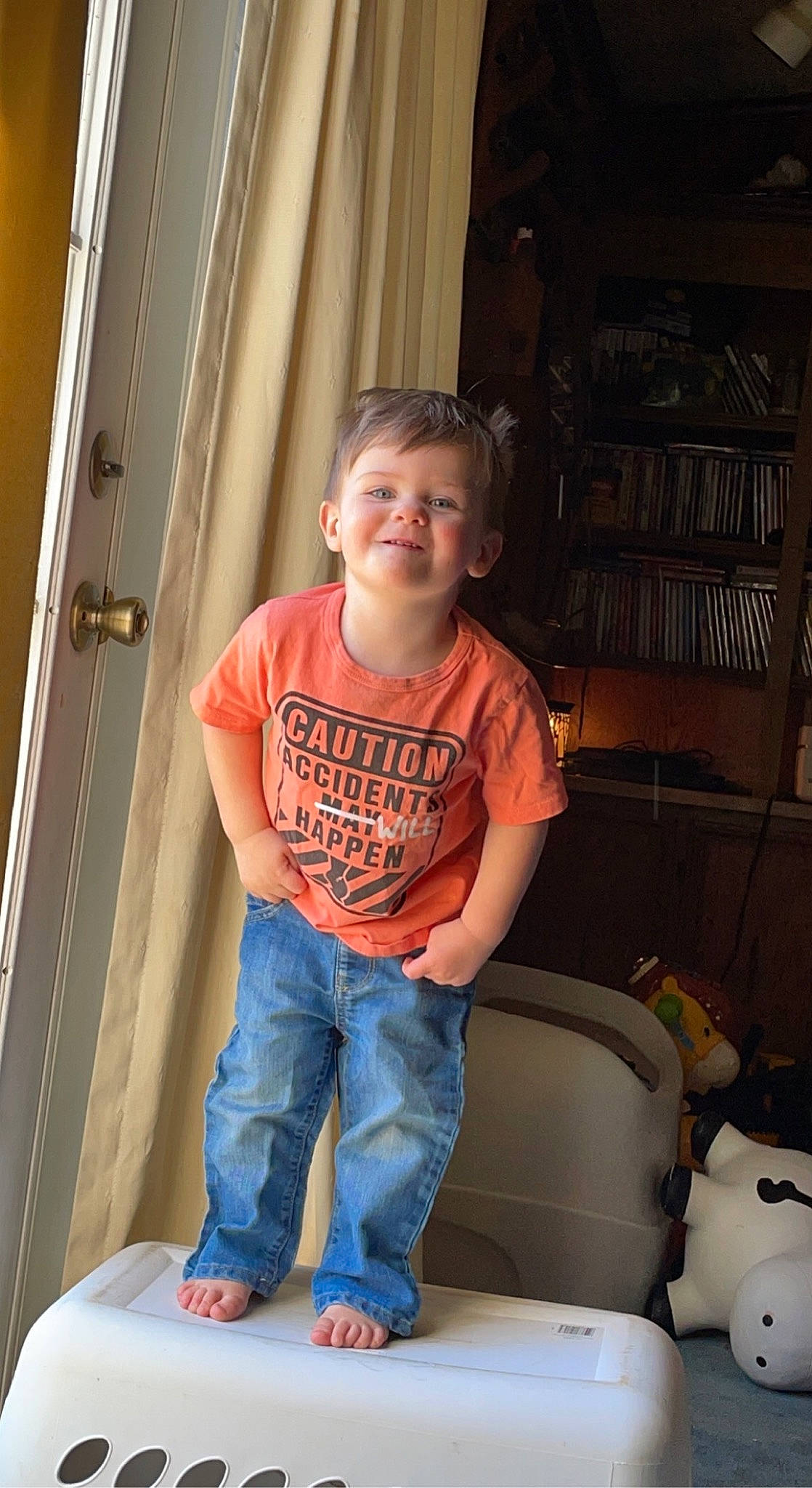 Jd is registered to the contest to win money with this photo: baby_toddler_clothing, bookcase, child, comfort, denim, elbow, fun, jeans, joy, lap, leisure, person, room, shelf, sitting, sleeve, smile, standing, t_shirt, thigh