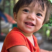 Max is registered to the contest to win money with this photo: child, toddler, smiling, face, eyes, hair, orange_shirt, skin, happy, portrait, indoors, closeup, expression, cute, person, young_child, cheerful, background_blur, clothing, baby