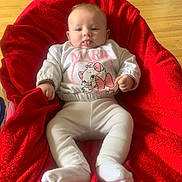 Inaya a rejoint le concours — aidez-le/la à gagner de superbes lots ! baby, infant, child, red_blanket, white_socks, cartoon_sweater, tongue_out, wooden_floor, cozy, cute, playful, indoor, smiling, sitting, person, face, clothing, plush, comfortable, young