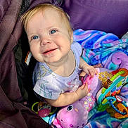 Victoria is registered to the contest to win money with this photo: baby, child, smiling, blue_eyes, blanket, toy, purple, colorful, playful, happy, infant, cute, portrait, indoors, fabric, soft, clothing, hand, face, toddler