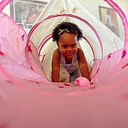 Kehlani is registered to the contest to win money with this photo: bow, child, crawling, curly_hair, cute, decor, face, happy, home, indoor, person, pink, play, play_tunnel, portrait, smiling, stars, tent, toddler, toy