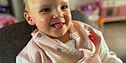 Mya participe au concours pour gagner de l'argent avec cette photo : toddler, child, smiling, tongue_out, pink_jacket, white_shirt, high_chair, indoor, face, cute, happy, person, baby, seatbelt, furniture, toy, background_blur, clothing, portrait, expression