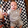 baby, child, infant, lying_down, portrait, face, wide_eyed, outfit, overalls, gray_clothing, checkerboard, mat, wooden_table, indoor, home, arms, legs, smiling, bottle, household_items