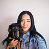 animal, black_and_tan, bright_lighting, closeup, companion, denim_jacket, dog, face, floppy_ears, holding, indoors, long_hair, pale_background, person, pet, portrait, puppy, selfie, smiling, woman