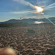 Marley participe au concours pour gagner de l'argent avec cette photo : beach, clouds, dog, footwear, mountains, nature, outdoor, person, relaxing, rocks, sand, sea, shoe, shore, sky, socks, sun, sunflare, sunlight, water