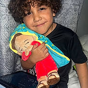 Santiago is registered to the contest to win money with this photo: child, curly_hair, smile, plush_doll, tablet, black_shirt, blue_jeans, bed, curtain, indoor, seated, toy, happy, portrait, person, furniture, hand, cuddling, casual, home
