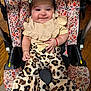 baby, infant, car_seat, floral_pattern, clothing, smile, face, hair_bow, leopard_print, pants, sitting, cute, child, indoors, wood_floor, red_bracelet, frilly_top, fashion, portrait, happy