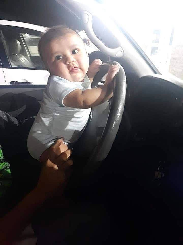 Bear is registered to the contest to win money with this photo: auto_part, automotive_exterior, automotive_window_part, baby, car, car_seat, child, driving, family_car, fun, person, smile, steering_part, steering_wheel, toddler, vacation, vehicle, vehicle_door