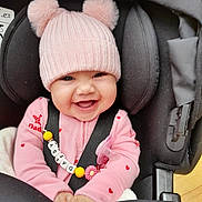 Daisy is registered to the contest to win money with this photo: accessory, baby, baby_clothing, car_seat, child, close_up, cute, happy, heart_pattern, indoors, infant, knitwear, pacifier, person, pink, pink_hat, pom_poms, seatbelt, smiling, toy