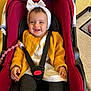 baby, car_seat, child, smiling, headband, jacket, white_clothing, black_strap, pink_pacifier_clip, footwear, indoor, floor, toy, happy, person, infant, seatbelt, toddler, cute, sitting