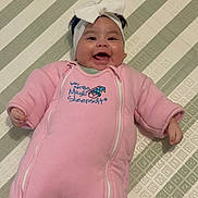 Dayamberly Garcia is registered to the contest to win money with this photo: baby, child, smiling, happy, portrait, lying_down, pink_outfit, onesie, headband, bow, blanket, bed, indoor, infant, face, hands, clothing, patterned_background, sleepwear, cute