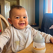 Tao participe au concours pour gagner de l'argent avec cette photo : baby, smiling, high_chair, bottle, bib, table, indoor, child, cute, happy, feeding, wooden_furniture, person, face, infant, milk_bottle, casual_clothing, home, portrait, early_childhood