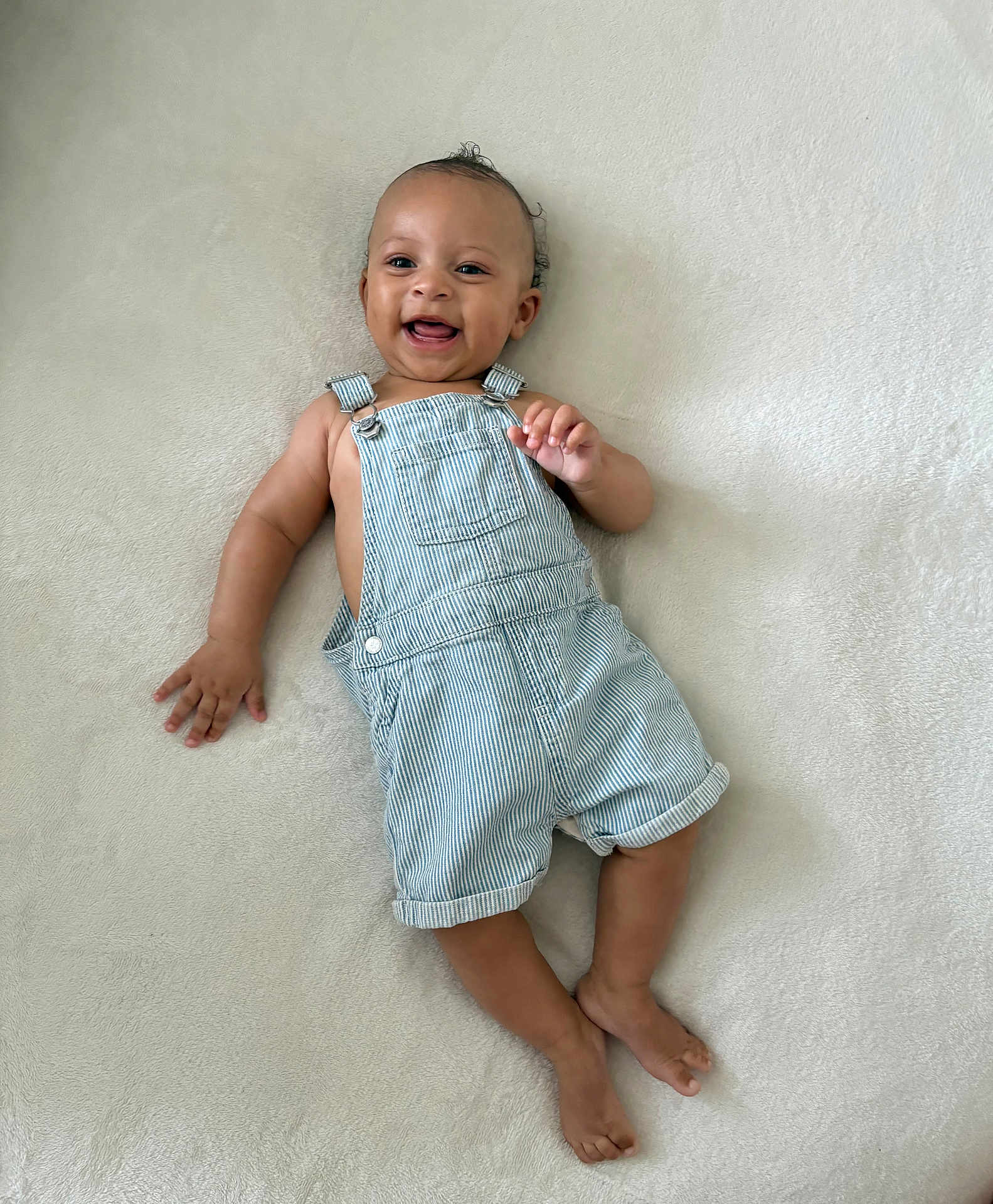 Isa Elah Raah joined the competition — help win amazing prizes! baby, smiling, overalls, striped_clothing, lying_down, infant, cute, happy, curly_hair, barefoot, light_background, one_person, child, skin, portrait, indoors, soft_texture, baby_clothes, young_child, joyful
