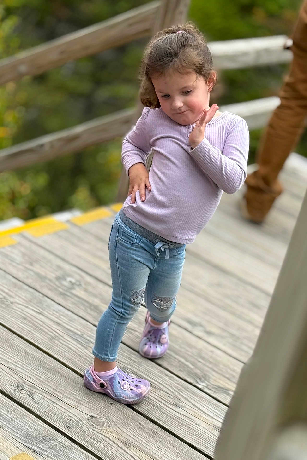 Harper is registered to the contest to win money with this photo: child, toddler, girl, pose, purple_shoes, crocs, jeans, long_sleeve, pink_top, wooden_deck, railing, outdoor, portrait, cute, playful, smile, casual_clothing, blurred_background, shallow_depth_of_field, person