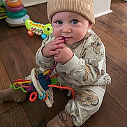 Carson is registered to the contest to win money with this photo: baby, child, hat, beige, ears, toy, colorful, floor, wooden_floor, sitting, clothing, cute, indoor, playful, infant, person, blue_eyes, long_sleeves, socks, smiling