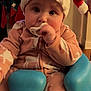 baby, santa_hat, pacifier, blue_baby_seat, reindeer_pajamas, holiday_decor, stockings, fireplace, television, indoor, child, cute, cozy, festive, infant, face, person, seated, home, holiday
