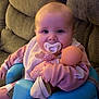 baby, pacifier, doll, blue_baby_seat, pink_outfit, couch, indoor, child, infant, cute, soft_lighting, seated, cozy, plush, smiling, portrait, home, small_toy, warm_colors, happy
