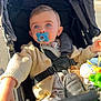 baby, baby_toy, blue_eyes, child, clothing, cute, expression, face, hand, infant, knit_cardigan, outdoor, pacifier, person, portrait, safety_harness, seat, stroller, sunlight, toy
