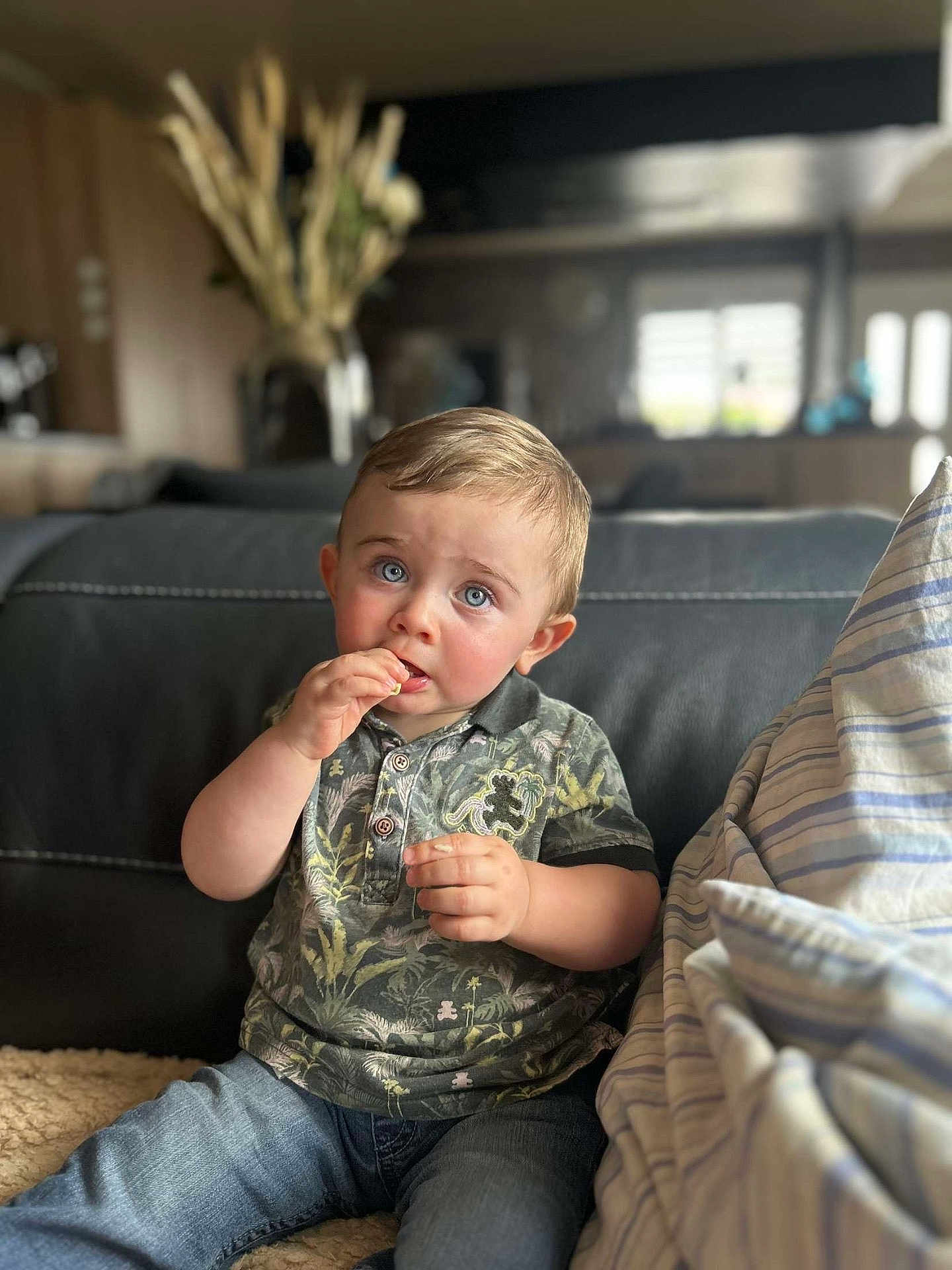 Mélio participe au concours pour gagner de l'argent avec cette photo : blue_eyes, casual_clothing, child, couch, curious, cushion, expression, face, furniture, home, indoor, jeans, person, polo_shirt, portrait, sitting, snack, soft_lighting, toddler, young_child