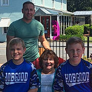 Ethan Zachary is registered to the contest to win money with this photo: family, portrait, boys, man, woman, outdoor, smiling, sports_jersey, blue_clothing, fence, building, window, greenery, sunlight, casual, people, group, street, daytime, happy