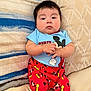 baby, infant, child, onesie, mickey_mouse, red_pants, sneakers, bracelet, pillow, bedding, headboard, couch, sitting, portrait, chubby_cheeks, dark_hair, cute, indoor, relaxed, clothing