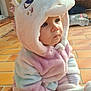 baby, toddler, child, unicorn, costume, hood, plush, onesie, sitting, tiles, terrace, sunlight, outdoor, portrait, cheeks, eyes, hand, cozy, pastel_colors, cute