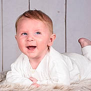 Raphaël a rejoint le concours — aidez-le/la à gagner de superbes lots ! baby, blue_eyes, child, cozy, cute, face, feet, fur_rug, hands, happy, indoor, infant, lying_down, portrait, smiling, soft_texture, toddler, warm, white_clothing, wooden_background