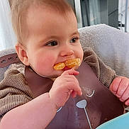 Louise participe au concours pour gagner de l'argent avec cette photo : baby, child, high_chair, bib, orange_slice, eating, kitchen, table, plate, hair, face, hand, food, indoor, cute, expression, person, young_child, feeding, smile