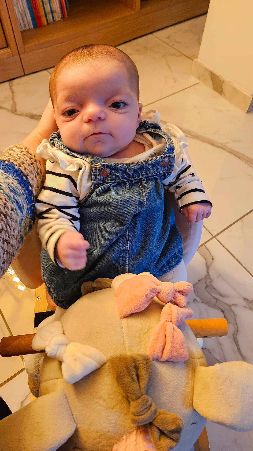 Katalïya a rejoint le concours — aidez-le/la à gagner de superbes lots ! baby, bows, child, clothing, cute, denim_overall, face, floor_tiles, hand, holding, indoor, infant, person, plush_toy, portrait, seated, soft_toy, striped_shirt, wooden_furniture, young