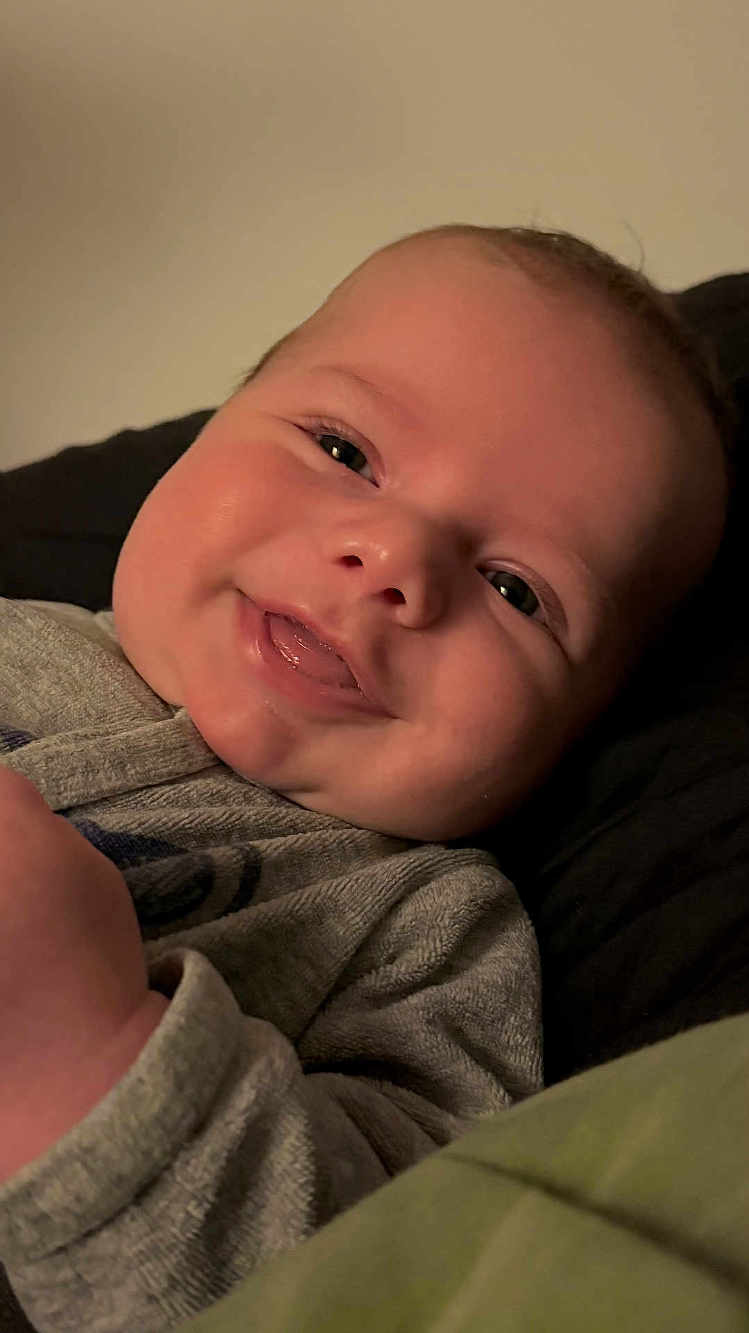 Rafaël a rejoint le concours — aidez-le/la à gagner de superbes lots ! baby, smiling, face, close_up, infant, tongue, eyes, skin, portrait, cozy, clothing, gray_outfit, soft, lying_down, cute, happy, child, young, indoors, warm_lighting