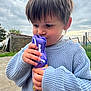 Ilyandro participe au concours pour gagner de l'argent avec cette photo : child, toddler, sweater, purple, chocolate, foil, outdoor, cloudy_sky, grass, shed, fence, curly_hair, holding, close_up, person, cute, snack, toy, garden, curious