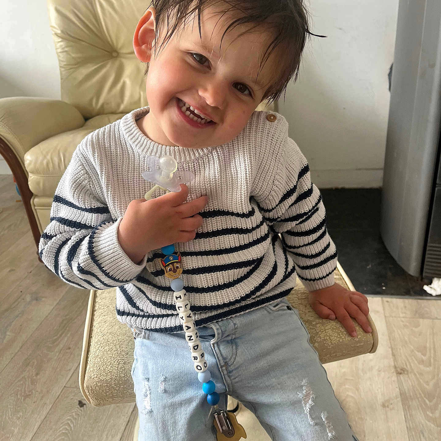 Ilyandro participe au concours pour gagner de l'argent avec cette photo : beads, casual_clothing, chair, child, cute, furniture, happy, indoor, jeans, living_room, pacifier, person, playful, seated, smiling, striped_clothing, sweater, toddler, wet_hair, wooden_floor