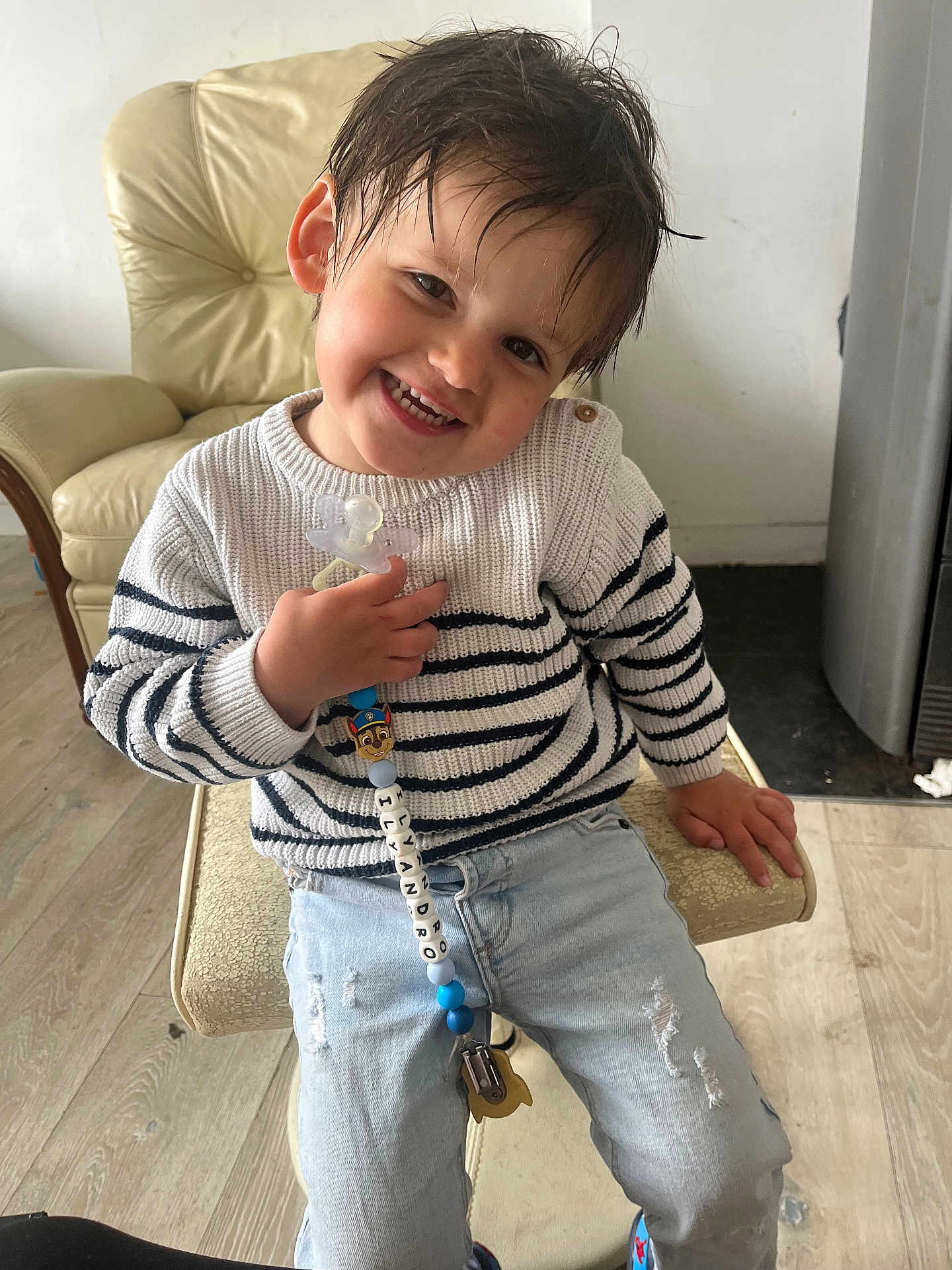 Ilyandro participe au concours pour gagner de l'argent avec cette photo : child, toddler, smiling, sweater, striped_clothing, jeans, pacifier, beads, chair, indoor, wooden_floor, happy, cute, wet_hair, person, furniture, living_room, casual_clothing, seated, playful