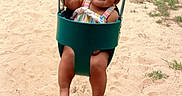 Skyelenna is registered to the contest to win money with this photo: toddler, child, swing, playground, sand, grass, smile, happy, outdoor, summer, yellow_chain, green_swing, footprints, tree, house, person, casual_clothing, baby, play, fun