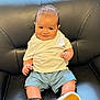 Gerald is registered to the contest to win money with this photo: baby, child, smiling, sitting, white_tshirt, blue_shorts, sneakers, leather_couch, window, blinds, indoor, natural_light, cute, portrait, infant, happy, person, footwear, young_child, casual_clothing