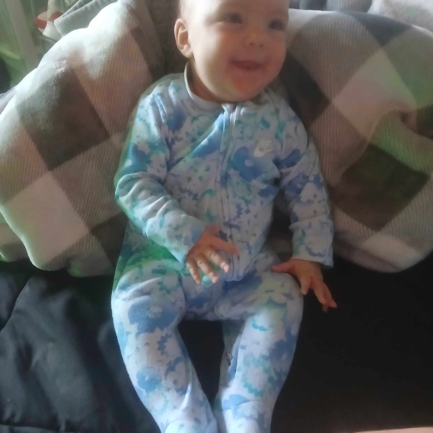 Adyson is registered to the contest to win money with this photo: baby, blanket, child, comfort, couch, cozy, face, floral_pattern, footed_pajamas, hand, happy, home, indoor, infant, onesie, person, plaid, seated, smiling, soft_lighting