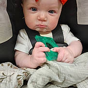 Honesty is registered to the contest to win money with this photo: baby, infant, child, car_seat, orange_bow, toy, blanket, pout, face, hands, clothing, seatbelt, indoors, cute, portrait, expression, human, sitting, closeup, young