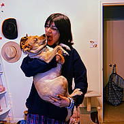 Melody is registered to the contest to win money with this photo: person, dog, indoor, holding, playful, expression, hat, wall_decor, plaid_pants, bracelet, cat_tree, doorway, floor, shelf, curious, casual_clothing, pet, interaction, home, room