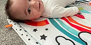 Luca is registered to the contest to win money with this photo: baby, infant, playmat, carpet, smiling, indoor, toy, colorful, rainbow, stars, white_clothing, floor, child, happy, person, head, face, crawling, play, home