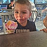 child, boy, ice_cream, cone, dessert, smiling, eating, food, cafe, restaurant, outdoor, sunlight, table, chair, window, blinds, background_people, portrait, puma_shirt, happy