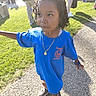 child, blue_tshirt, grass, outdoor, daylight, path, people, crowd, necklace, curly_hair, watch, sneakers, standing, sunlight, casual_clothing, park, portrait, young, person, walking