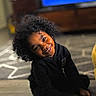 Jaheim is registered to the contest to win money with this photo: black_clothing, casual, child, cozy, curly_hair, cute, face, floor, furniture, happy, home, indoor, living_room, person, portrait, sitting, smiling, tilted_head, wood_floor, young