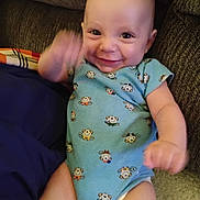 Calvin is registered to the contest to win money with this photo: baby, infant, smiling, blue_onesie, monkey_print, couch, brown_fabric, happy, waving, motion_blur, indoors, child, person, cute, seated, plush, arm_movement, head, face, expression