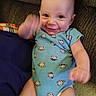 baby, infant, smiling, blue_onesie, monkey_print, couch, brown_fabric, happy, waving, motion_blur, indoors, child, person, cute, seated, plush, arm_movement, head, face, expression